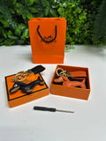 Two leather teckle keychains in orange  boxes with an orange bag in the background.