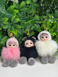 Three small dolls with fluffy accessories against a green leafy background
