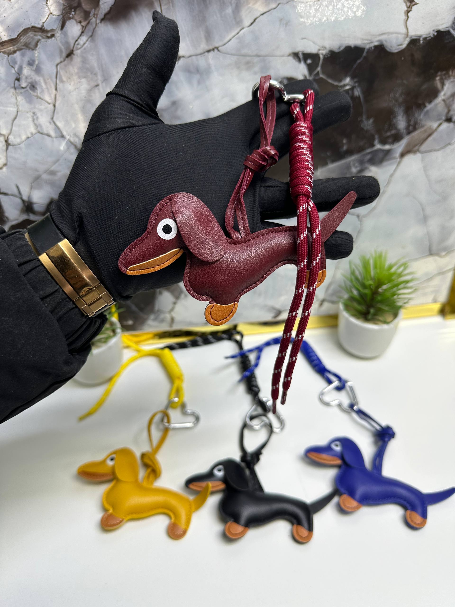 Hand holding a red dachshund-shaped keychain with more keychains in the background on a marble surface.