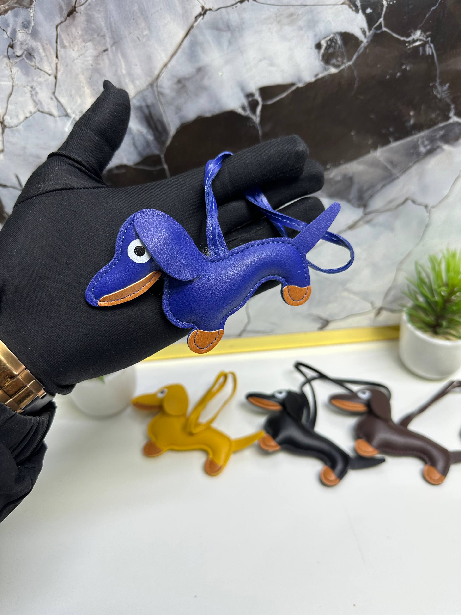 Blue dog-shaped keychain held by a gloved hand with other dog-shaped keychains in the background.
