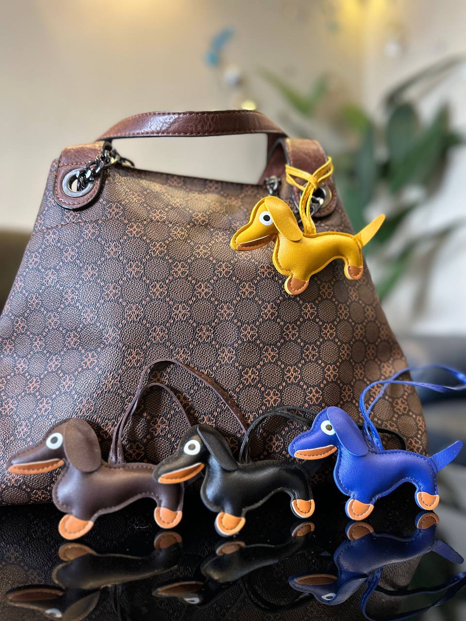 Gold dachshund-shaped keychain on a patterned handbag with four other dachshund-shaped keychains in front.