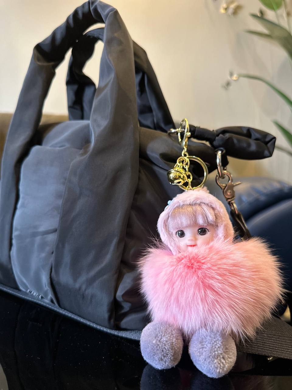 Keychain with a doll wearing a pink fluffy hood on a gray handbag.
